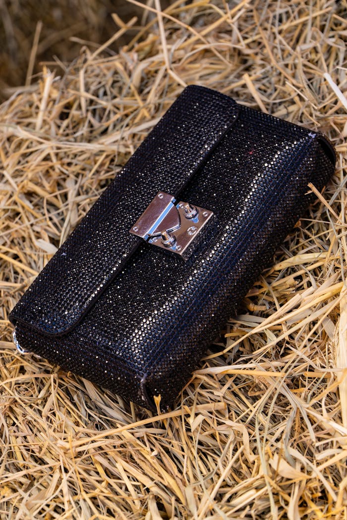 services-05 Stylish black clutch purse resting on straw, offering a rustic yet chic look.
